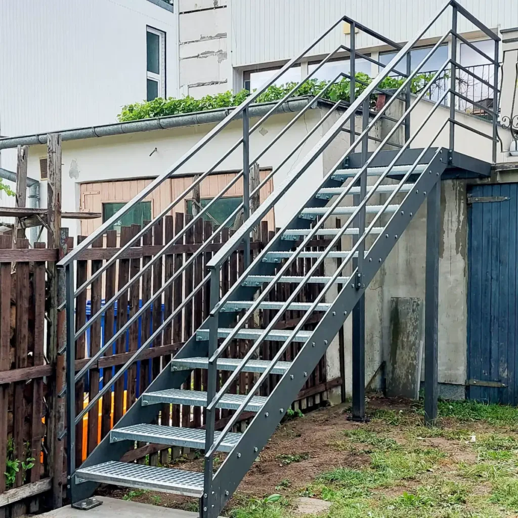 Schody zewnętrzne stalowe kratownicowe z metalowymi poręczami.