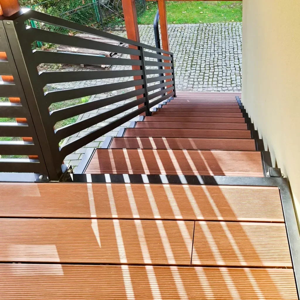 Drewniane stopnie schodów z metalowymi poręczami i drewniana podłoga na piętrze.